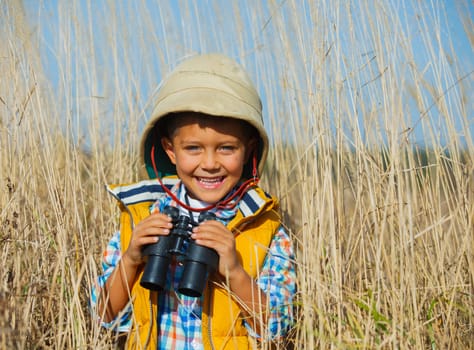 Young boy child playing pretend explorer adventure safari game outdoors with binoculars and bush hat