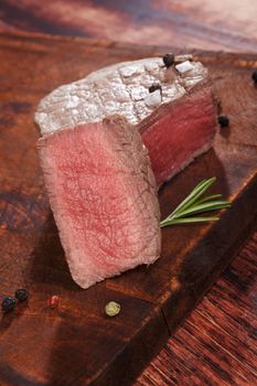 Steak eating. Rare tenderloin steak on wooden kitchen board with rosemary and peppercorns. Culinary beefsteak eating. 