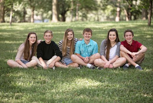 Row of six male and female teens sitting outside