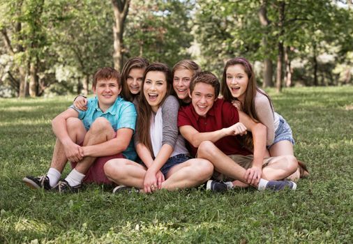 Happy group of European teenagers sitting on grass