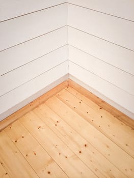 Empty room corner with wooden floor and white painted wall.