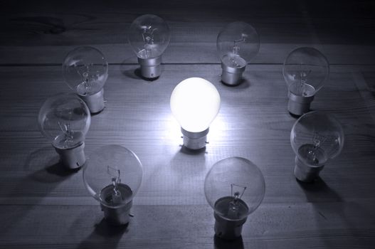 Illuminated light bulb in the centre of a circle of unlit lamps signifying uniqueness, innovation or leadership