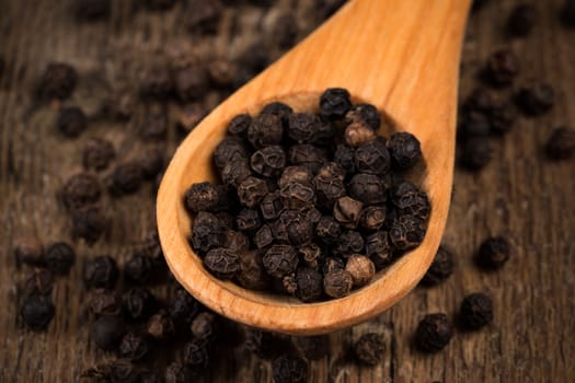 black pepper on wooden spoon and wood background