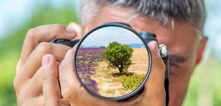 Photographer taking photo with DSLR camera at tree in countryside. Shallow DOF