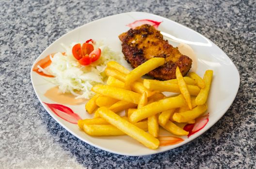 White plate with floral pattern on a schnitzel with chips and salad

