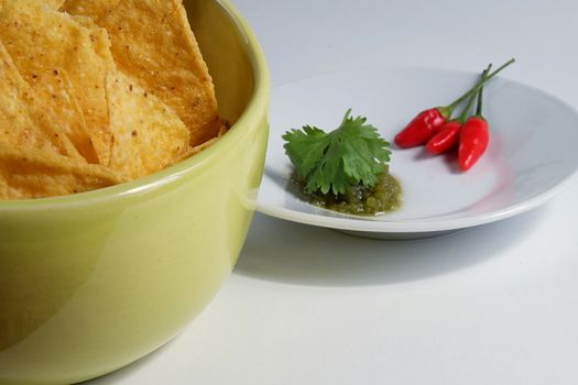 A green bowl of Mexican nachos with green sauce and red hot peppers on a dish. Tex-mex