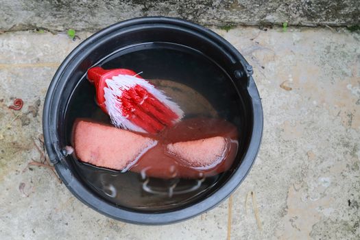 Plastic brush and sponge in a bucket of water.