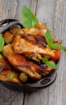 Homemade Roasted Chicken Thighs with Tomatoes, Green Olives and Basil in Black Fry Pan closeup on Rustic Wooden background