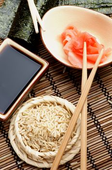 Ingredients to Preparing Sushi  with Nori, Ginger, Rice, Soy Sauce and Chopsticks on Bamboo Straw Mat. Top View