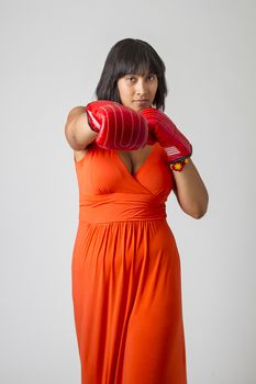 twenty something philipino woman, in low cut orange dress, throwing a punch with red boxing gloves