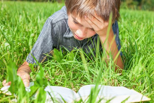 Boy lying in grass reading a book in a summer field