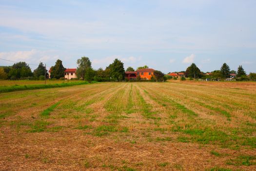 Field with house under cloudy blue sky