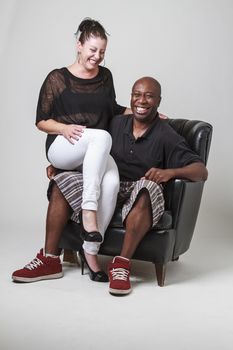 Caucasian woman sitting on a bald black man lap, laughing hard