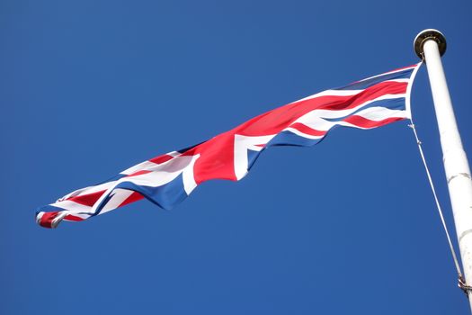 Union Jack flag on white flagpole with blue sky in background