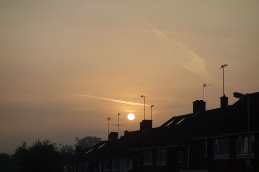 Early morning sun above row of suburban house roofs