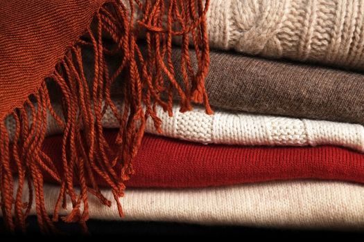 Several woolen sweaters stacked on top of each other and a scarf on top of them