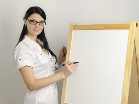 Working Girl in glasses writes a marker on a white board, looking at the camera. Studio, white background