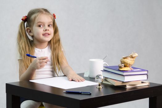 girl cheerfully and joyfully looks in the frame, sitting at the table. In one arm and the girls handle, which she is going to write on a sheet of paper. There are tombs of books, sheets of paper, a pen, glass globe, with a glass of tea, sea shell