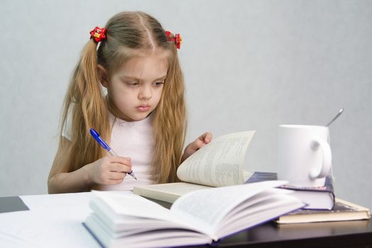 girl sits at a table and flips through the book and writes out the information you need. Next are still books, sheets of paper, a pen, a glass of tea. The image of a student, a pupil, a teacher and literary critic