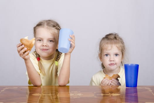 Two children sitting at the table, eating a muffin and drink of colored plastic cups