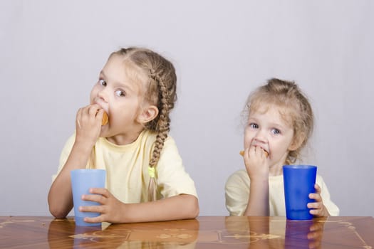 Two children sitting at the table, eating a muffin and drink of colored plastic cups