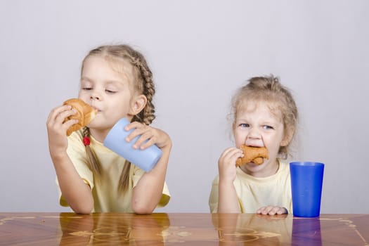 Two children sitting at the table, eating a muffin and drink of colored plastic cups