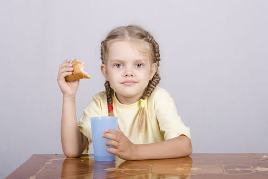 Four-year-old girl sitting at the table, eating a muffin and drinking from a plastic Cup