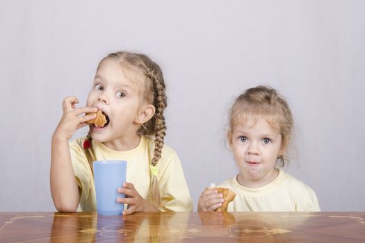 Two children sitting at the table, eating a muffin and drink of colored plastic cups