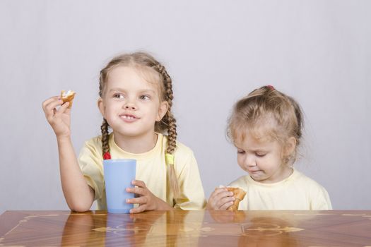 Two children sitting at the table, eating a muffin and drink of colored plastic cups