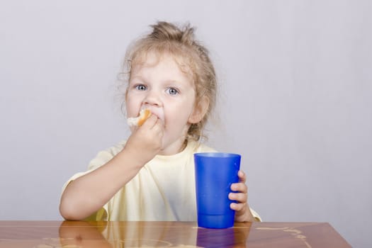 Two-year-old girl sitting at the table, eating a muffin and drinking from a plastic Cup