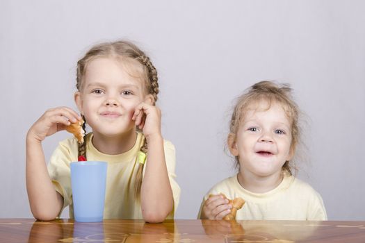 Two children sitting at the table, eating a muffin and drink of colored plastic cups