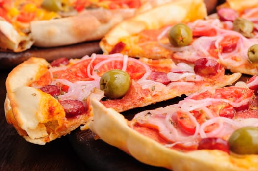 Closeup of pizza with tomato, salami, peppeeoni, olives and yellow hot pepper