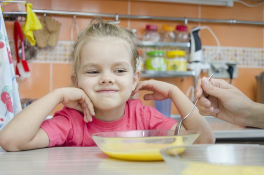 Girl five years eats porridge, sitting at the kitchen table.