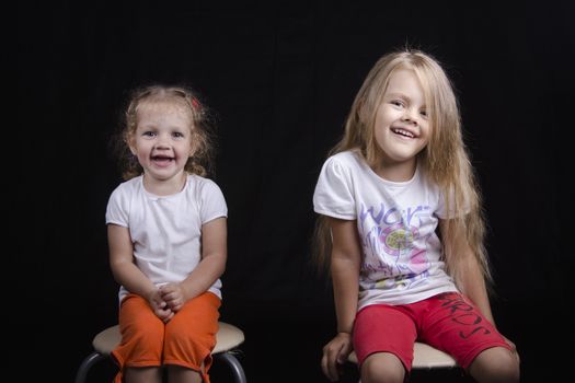 Portrait of the sisters - two little girls on the chairs. Girls fun smiling and looking in the frame.