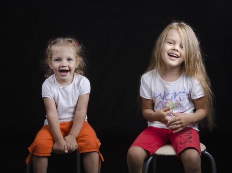 Portrait of the sisters - two little girls on the chairs. Girls fun smiling and looking in the frame.