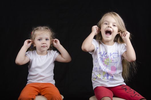 Portrait of the sisters - two little girls on the chairs. Girls fun smiling and looking in the frame. Girls hold hands behind your ears