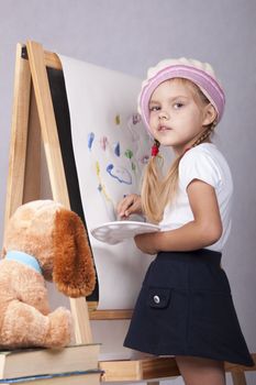 Four-year-old girl playing in the artist and draws on the easel-painting. In the arms of children brush and palette.