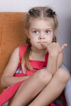 Girl sitting on couch. Girl with enthusiasm and thoughtfully looks slightly to left. one put a finger to his mouth