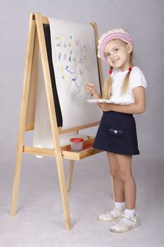 Four-year-old girl playing in the artist and draws on the easel-painting. In the arms of children brush and palette.