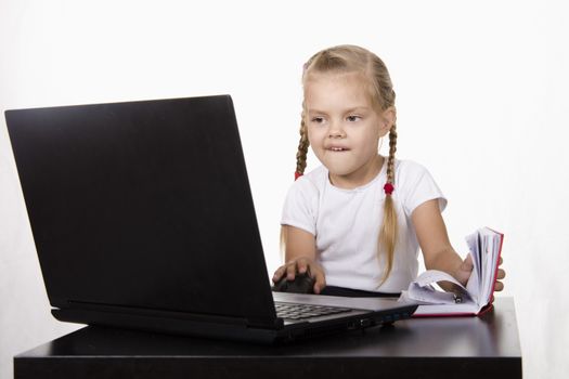 Image of a business girl. girl sitting at table. On table is a laptop, girl it works. girl joyfully looking into laptop other hand opens Notepad