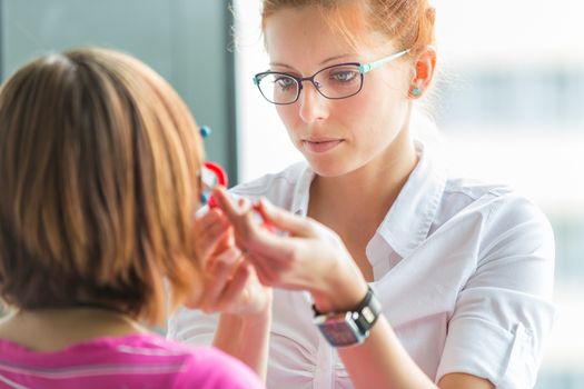 Optometry concept - pretty, young female optometrist examining her patient's eyes, finding the optimal correction to achieve optimal sight