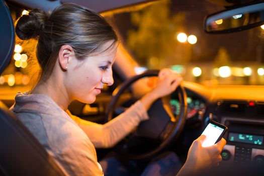 Pretty young woman using her smart phone while driving her car at night