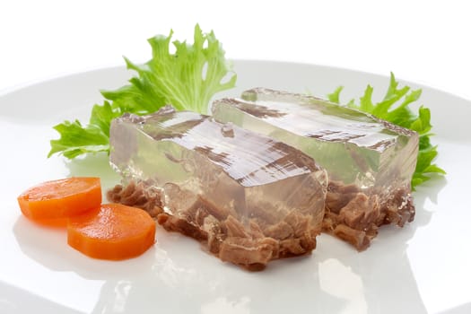 Two pieces of beef aspic with green fresh parsley and orange carrot on the white plate