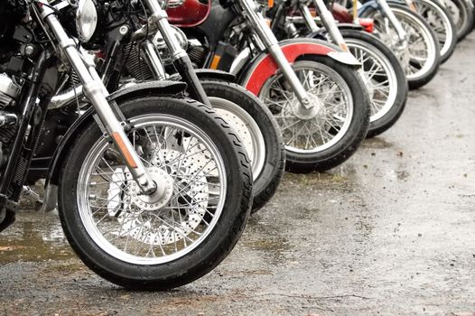 row of motorcycles parked together on a rainy day