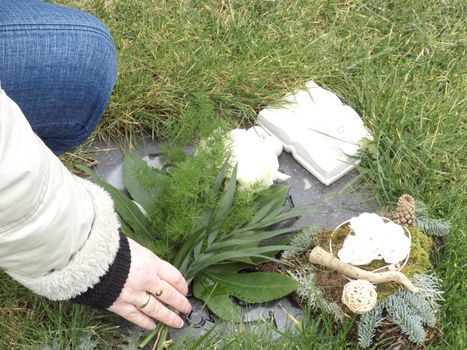 Hands of a woman stores the flowers on the grave