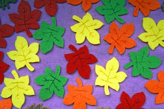 Yellow, red, orange and green Maple leaves out of felt on fabric as a background                                