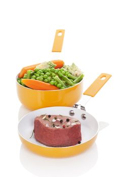 Big steak with steamed colorful vegetable in orange pan isolated on white background. Culinary delicious healthy meal.
