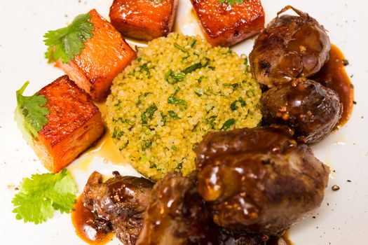 Organic meat of lamb cooked with slices of pumpkin and quinoa in oriental style on a white plate