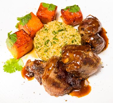 Organic meat of lamb cooked with slices of pumpkin and quinoa in oriental style on a white plate