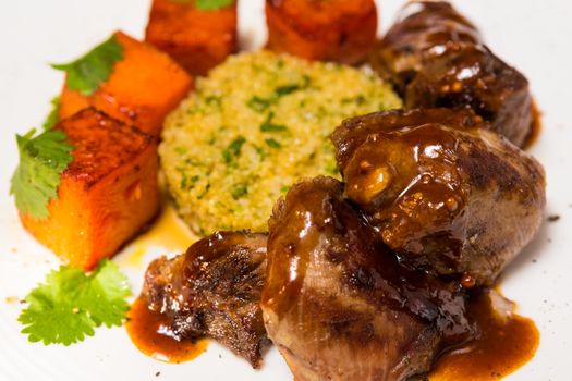 Organic meat of lamb cooked with slices of pumpkin and quinoa in oriental style on a white plate